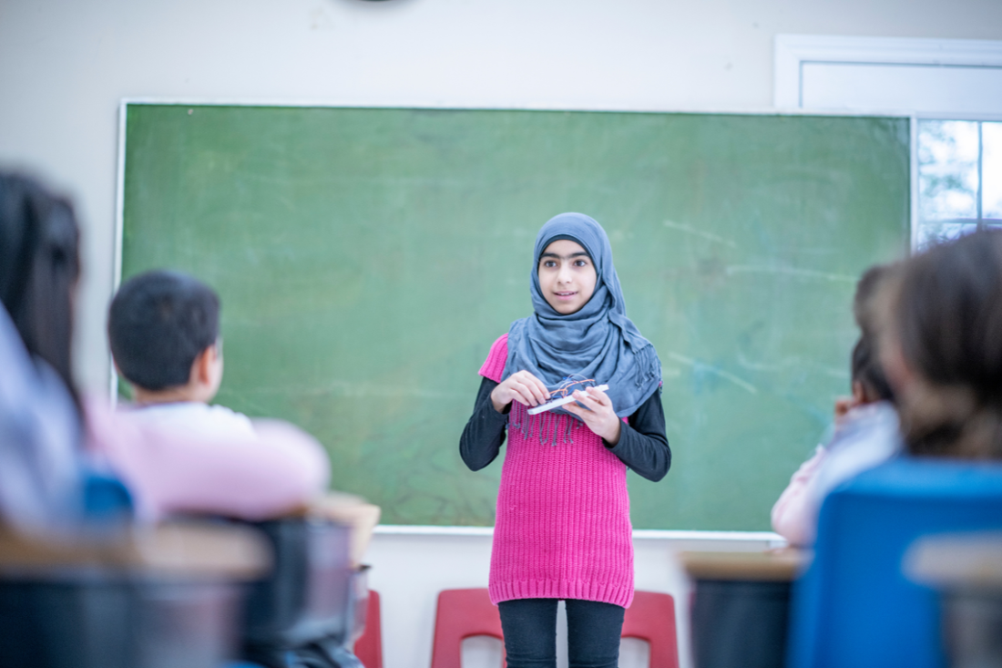 young student with headscarf standing up in front of the class showing minimal signs of anxiety