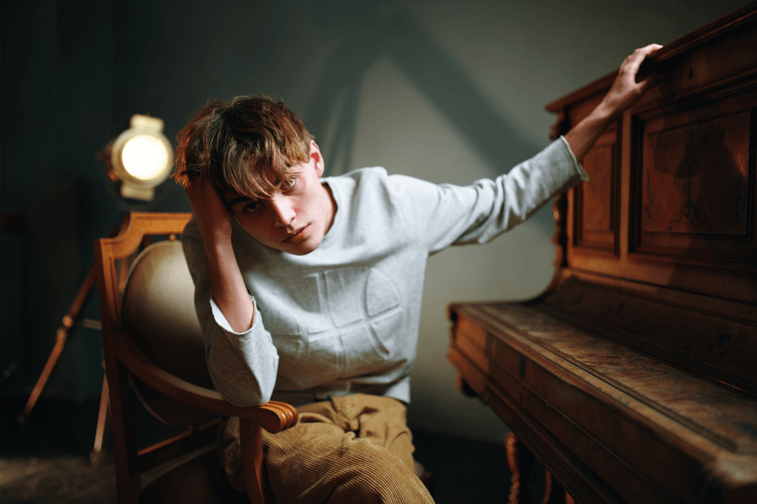 boy with head in one hand and touching piano with the other. He looks tired and stressed. the piano is closed.