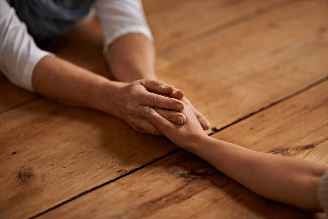 an older person holding a younger persons hand across a wooden table.  Showing connection.