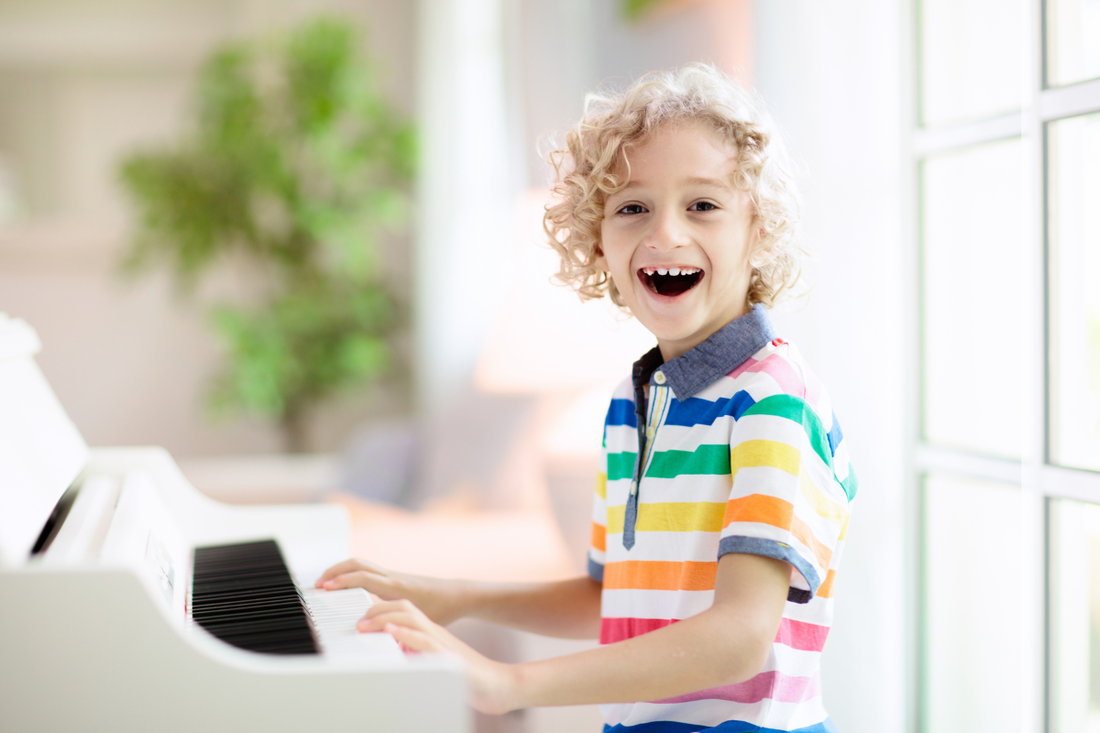 young boy with a big smile sitting in front of an open piano, showing pure joy.